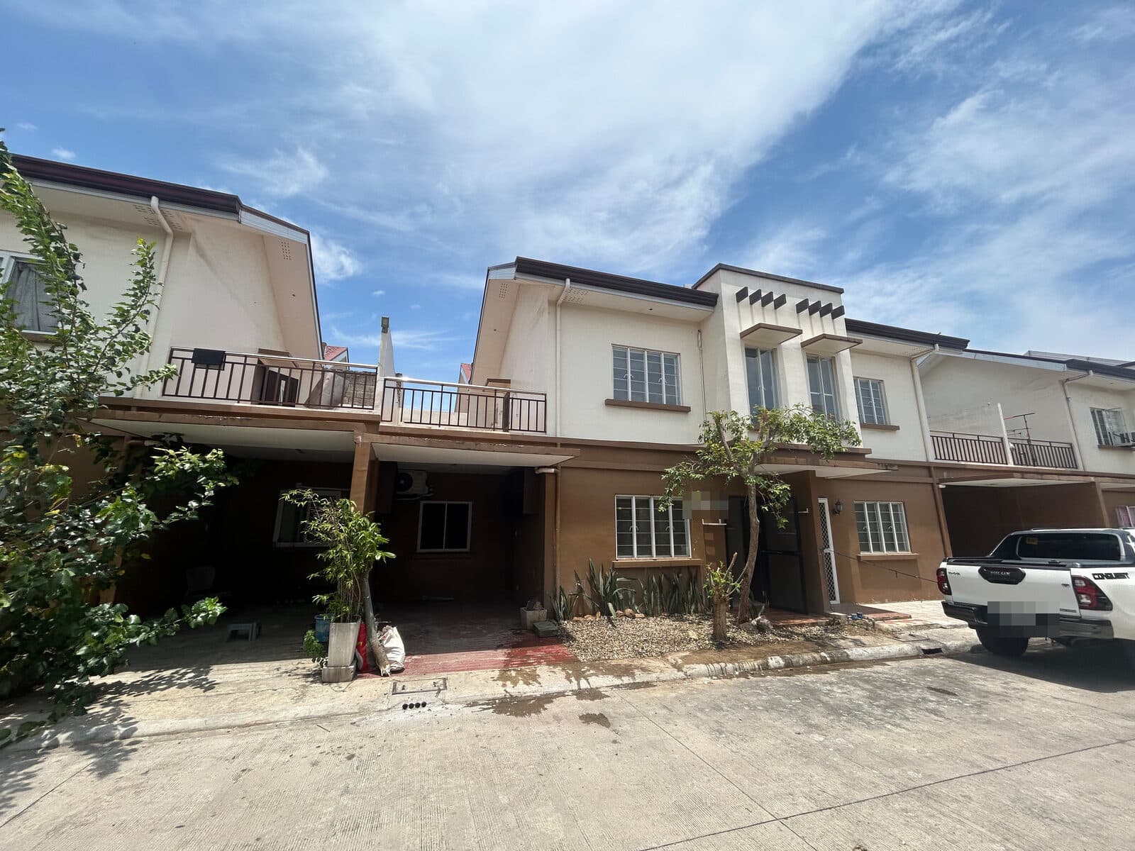 Row of two-storey residential townhouses across the subdivision road, with carports and small front plantings